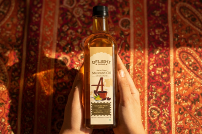 Cold-pressed yellow mustard oil bottle beside mustard seeds and brass oil press on wooden surface